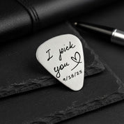 Personalized metal guitar pick resting on a black notebook, engraved with the phrase “I pick you” and a small heart plus special date, highlighting the brushed silver finish and smooth rounded edges. Custom engraved guitar pick for boyfriend, husband, fiancé or partner, a romantic anniversary, wedding or Valentine’s Day gift idea for musicians and music lovers, keepsake plectrum he can actually play.