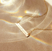 Gold necklace with a custom sonogram bar pendant on a textured beige surface