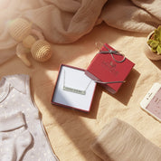 Personalized heartbeat bar necklace in sterling silver displayed in a red Danique Jewelry gift box, styled with soft baby essentials and warm natural lighting, symbolizing a meaningful gift for new mom, baby keepsake, or Mother’s Day jewelry.