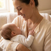 Mother holding newborn baby while wearing a delicate mama bird necklace with two baby bird charms. Meaningful family jewelry symbolizing motherhood, children, and love. Personalized gift for mom or new mother.