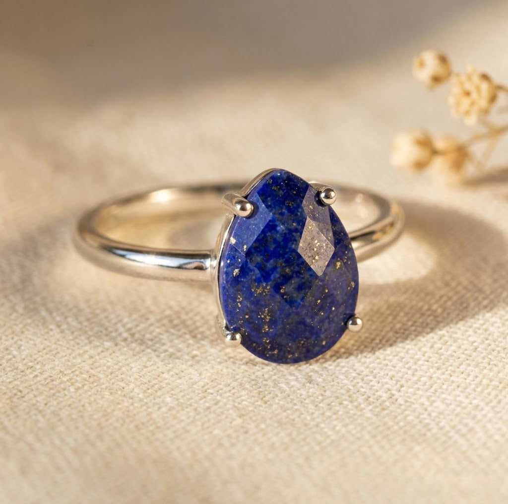 Close-up of lapis lazuli teardrop ring in sterling silver prong setting with faceted deep blue gemstone.