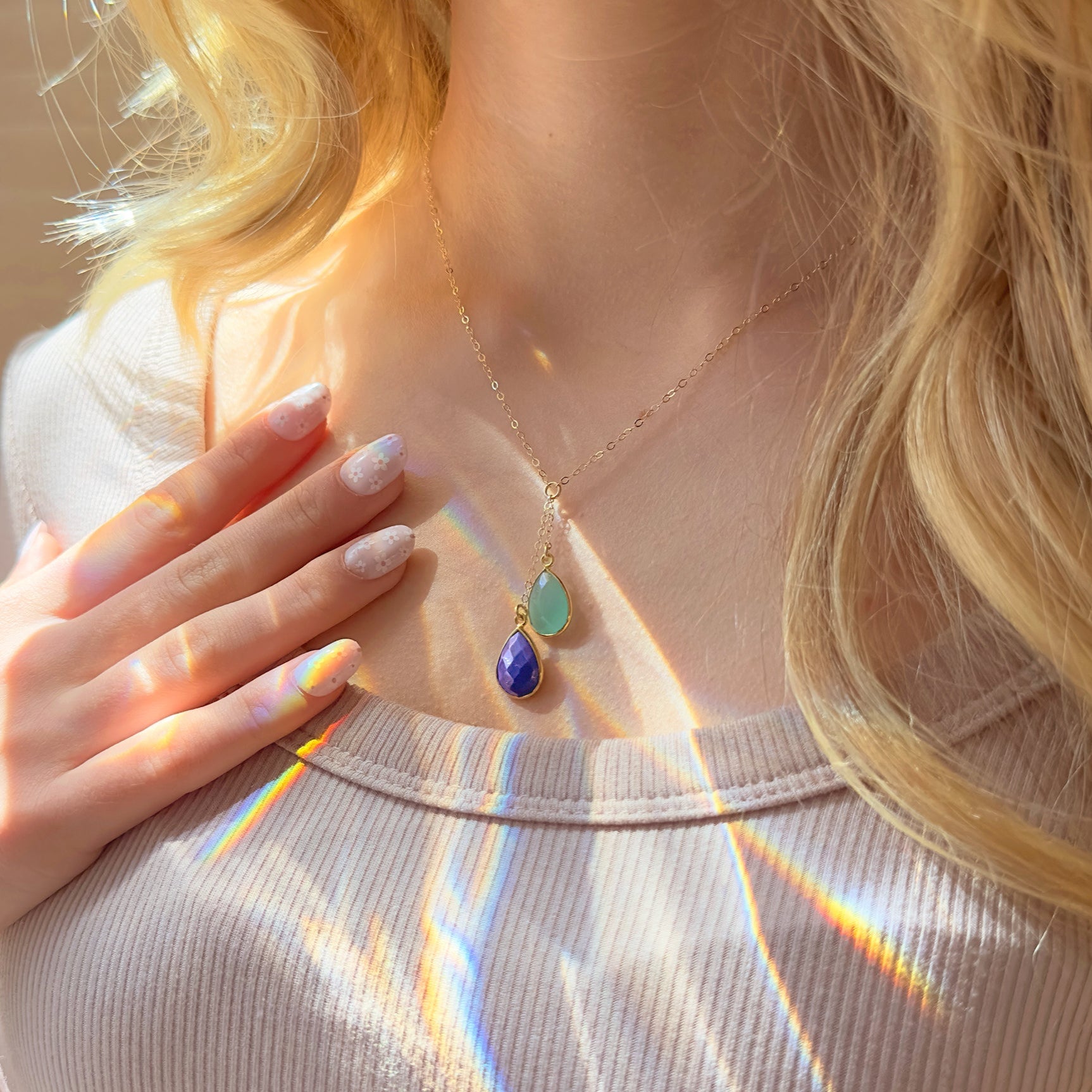 Close-up of a person wearing a necklace with colorful pendant, hand touching collarbone.