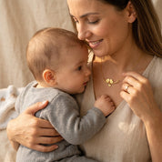 Mother holding her baby while wearing a personalized gold lovebirds necklace with a stamped family charm.