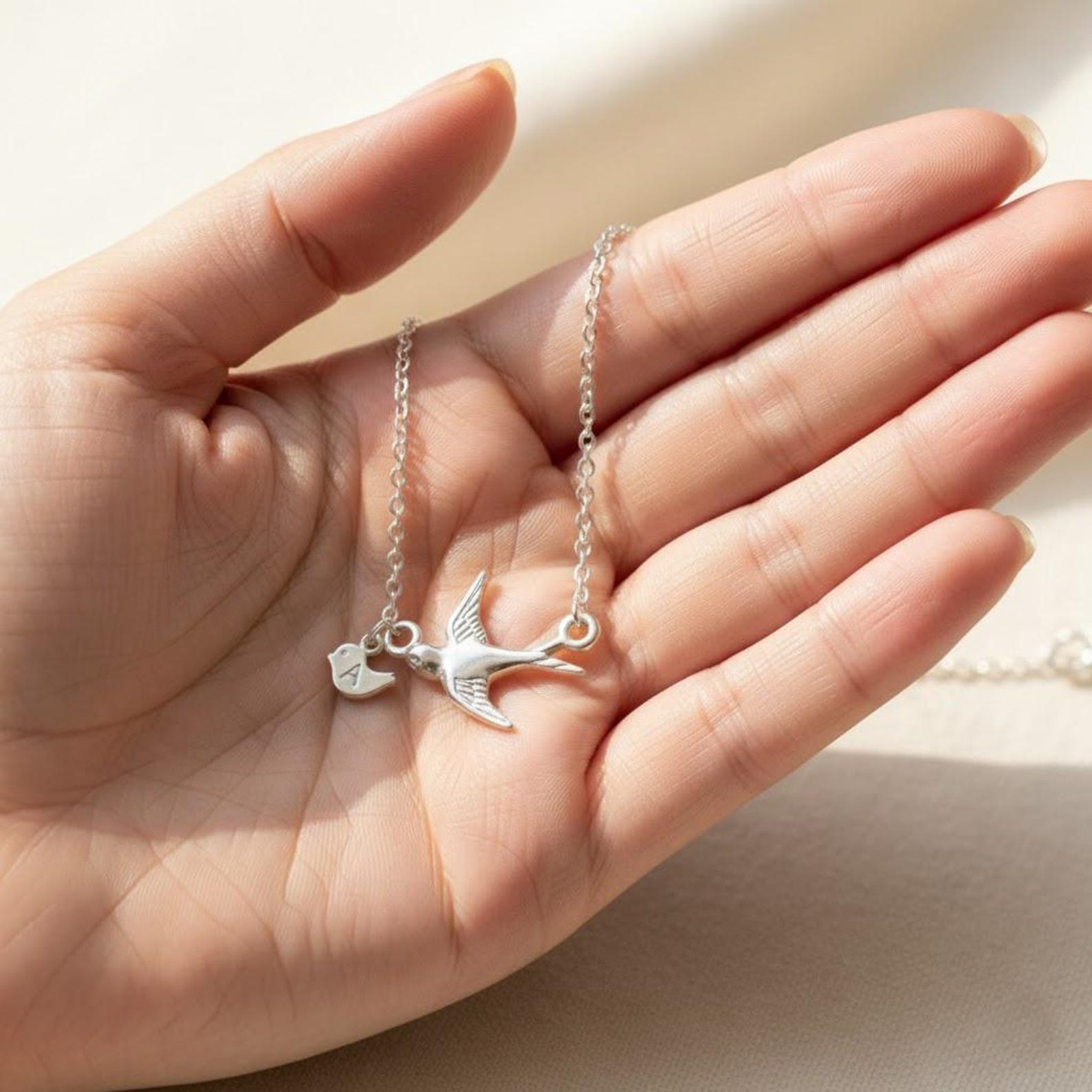 Silver mama bird necklace with tiny baby bird charm engraved with initial, resting in a woman’s hand. Delicate personalized family necklace symbolizing motherhood, love, and children.