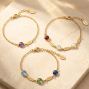Dainty personalized birthstone bracelet with one name charm displayed on soft neutral fabric.