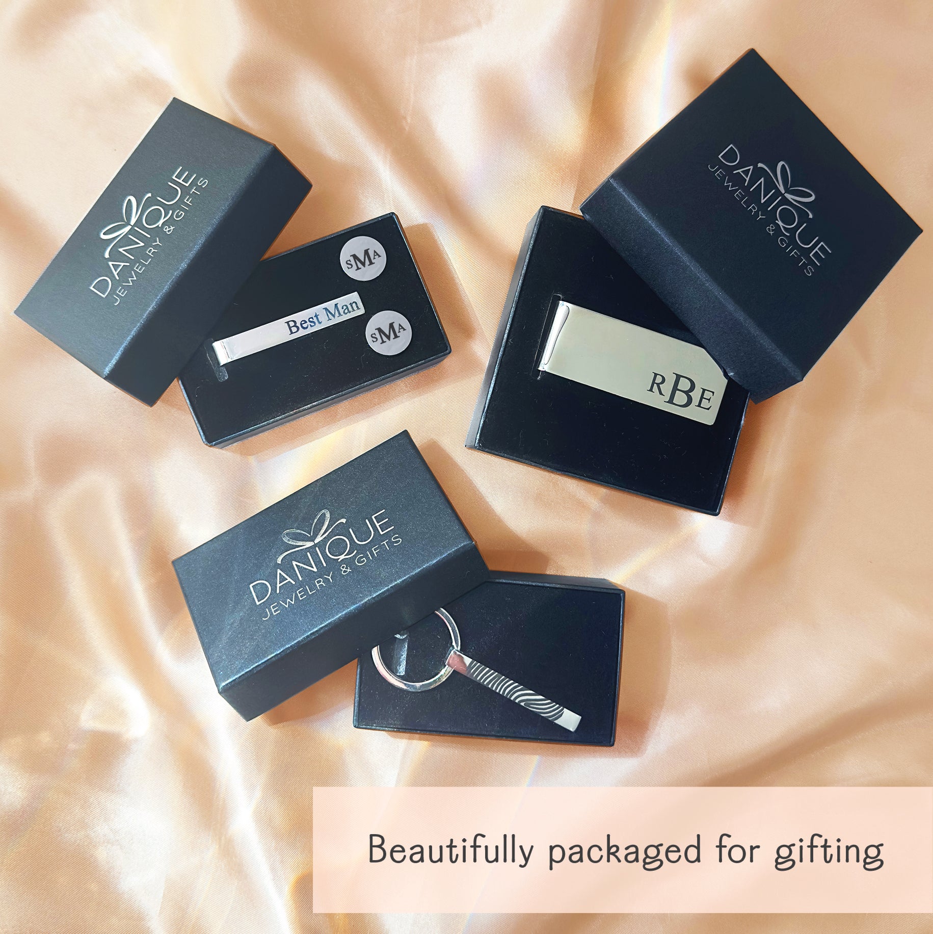 Personalized jewelry and accessories beautifully packaged for gifting, shown in elegant Danique Jewelry & Gifts branded boxes on soft satin fabric background. Gift-ready presentation featuring engraved tie clip, custom money clip, and personalized cufflinks displayed inside luxury black jewelry boxes. Ideal packaging for wedding gifts, groomsmen gifts, best man gifts, Father’s Day, anniversaries, and special occasions, with premium presentation designed to make gifting effortless and memorable.