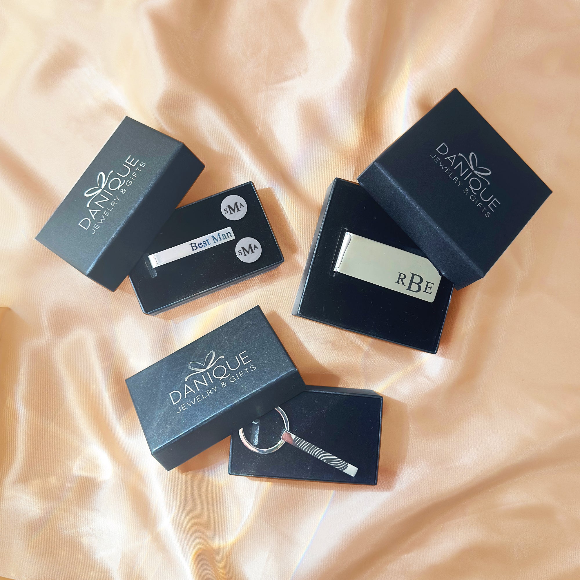 Gift-ready men’s accessories set on champagne satin: stainless steel tie slide, round initial cuff links, monogram money clip, and etched bar keychain, each in branded presentation boxes. Perfect for usher gifts, ring bearer thank-you, Father’s Day, retirement, corporate/executive gifts, birthday for husband, or Valentine’s gift for him. Custom initials with laser etching create a bespoke keepsake in a sleek, modern silver-tone style.