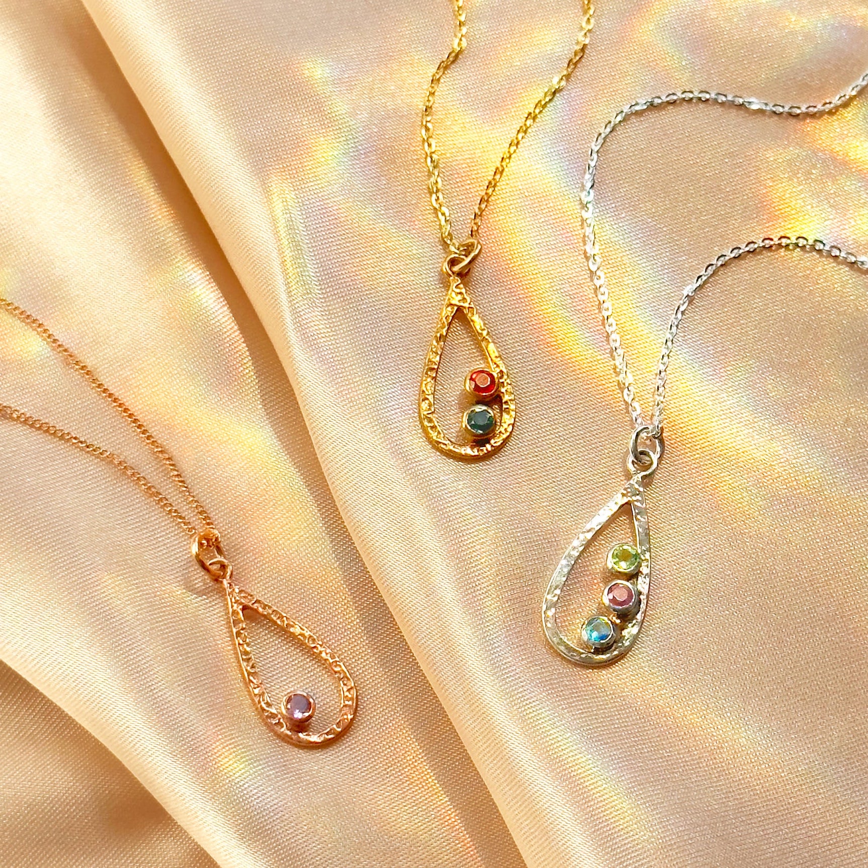 Custom birthstone necklace for mom in gold, rose gold, and sterling silver with teardrop pendant on soft satin background