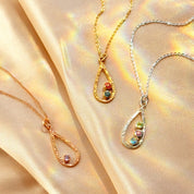 Custom birthstone necklace for mom in gold, rose gold, and sterling silver with teardrop pendant on soft satin background