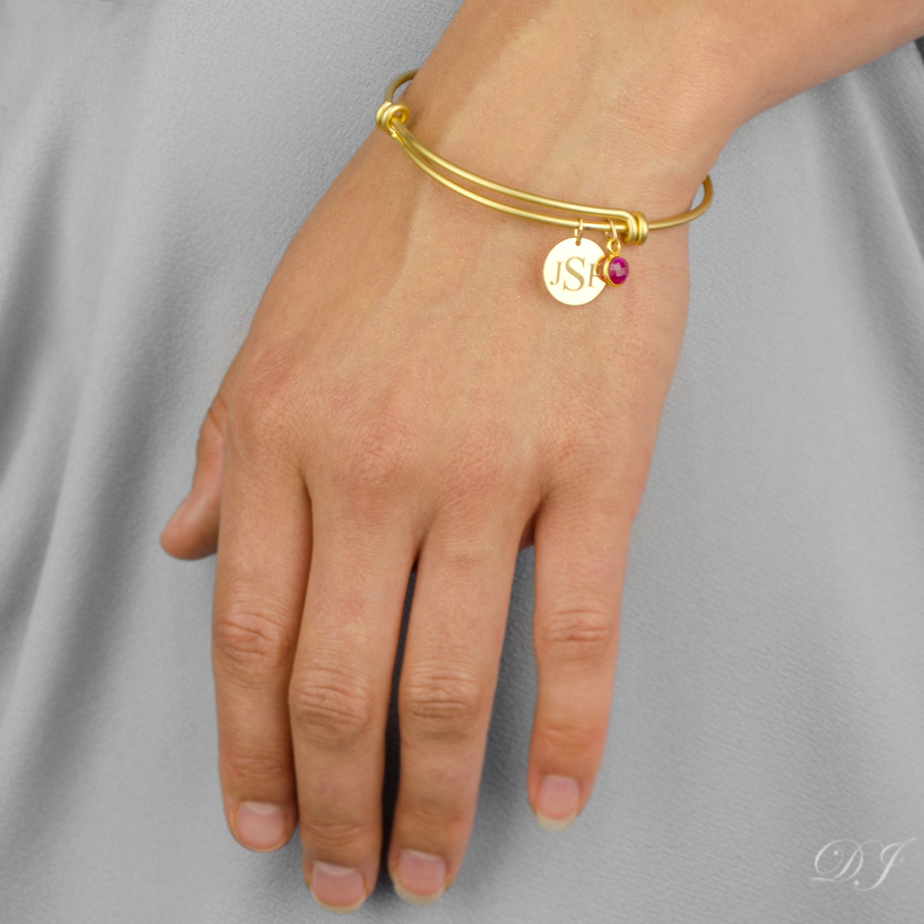 Model in gray dress is wearing the gold filled bangle with engraved disk and ruby birthstone. 