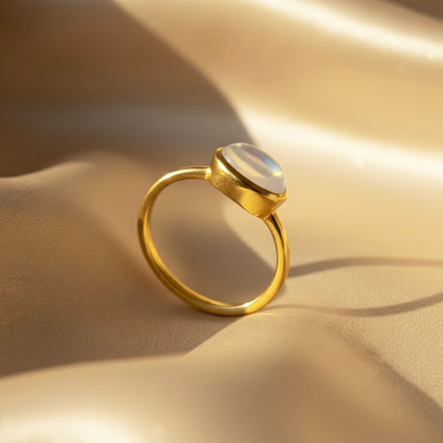 Stackable oval gemstone rings featuring rainbow moonstone and other colorful birthstones in gold settings.