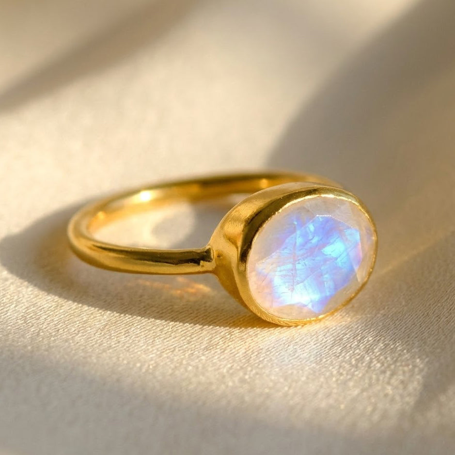 Oval bezel set moonstone ring in gold vermeil with rainbow flash on neutral background