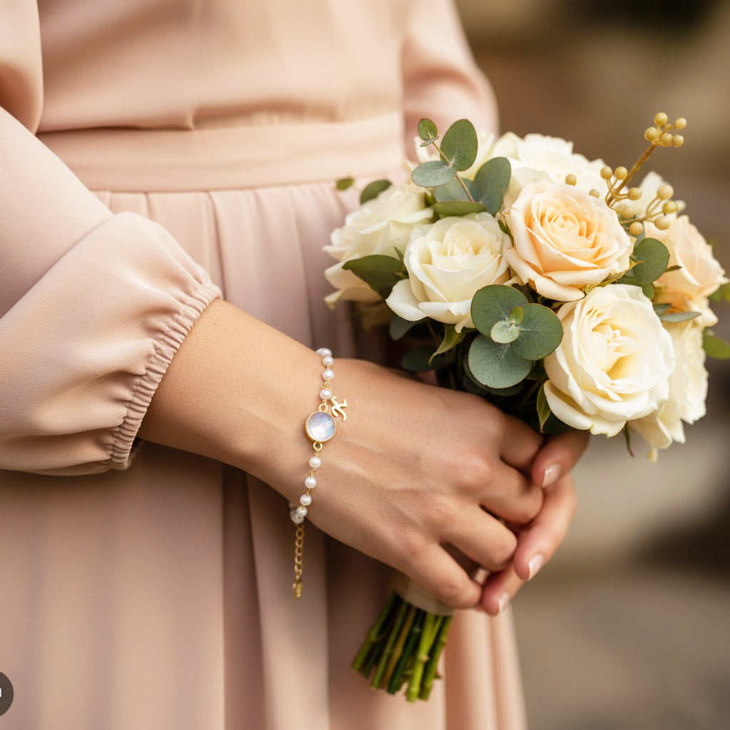 Bride wearing personalized initial and birthstone bracelet, June pearl and August peridot charms, elegant bridesmaid jewelry gift idea for wedding day, custom gold charm bracelet with initial letter and gemstone.