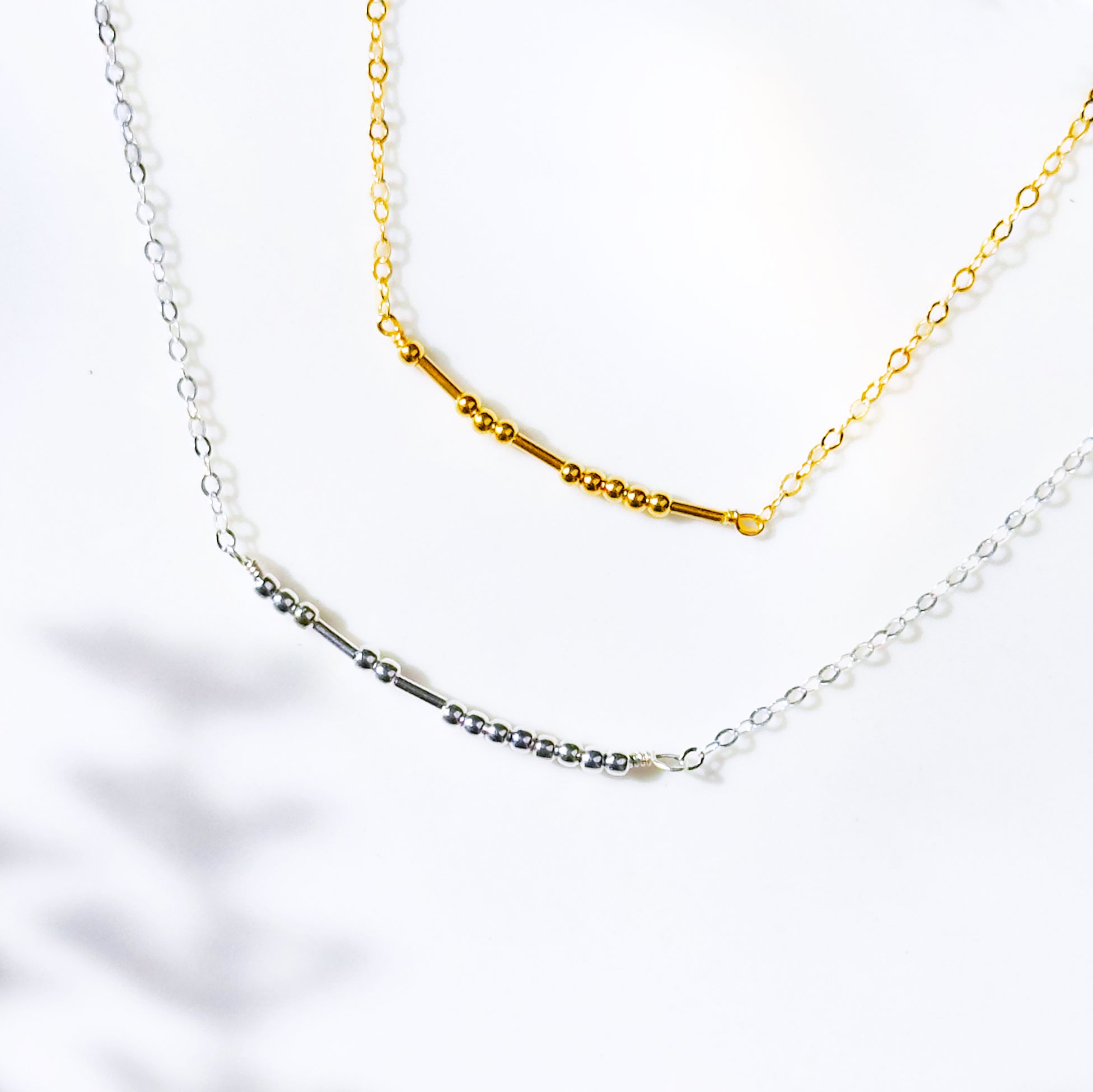 A gold filled and a sterling silver beaded morse code necklace layered on top of each other. These make perfect gifts for mothers with their children's name beaded in morse code. Couple gifts, couple initials, secret message gift, secret code gift, meaningful minimalist dainty necklaces for women, mothers day gift for her, personalized gift for women. Handmade beaded necklace gift. Custom beaded jewelry.