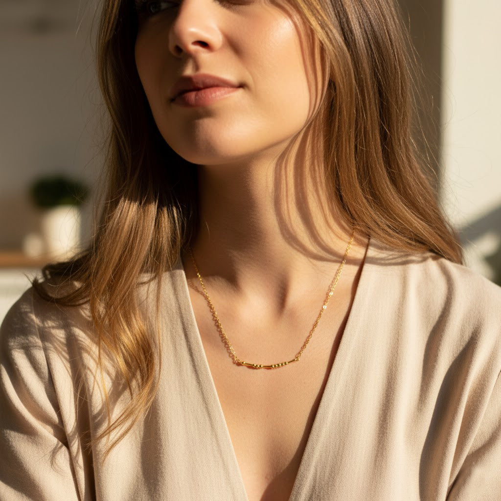 Model wears a subtle hidden message morse code necklace resting at the base of the neck, showing how the dainty bead pattern reads as chic minimalist jewelry from a distance. Choose gold filled or sterling silver for a refined friendship gift, birthday present, or daily layering piece. The adjustable 16–18 inch chain, lightweight feel, and handcrafted USA quality make this secret message necklace effortless and meaningful.