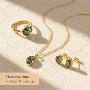 Moss agate and matching gemstone jewelry set with ring, necklace, and earrings displayed on soft beige fabric.