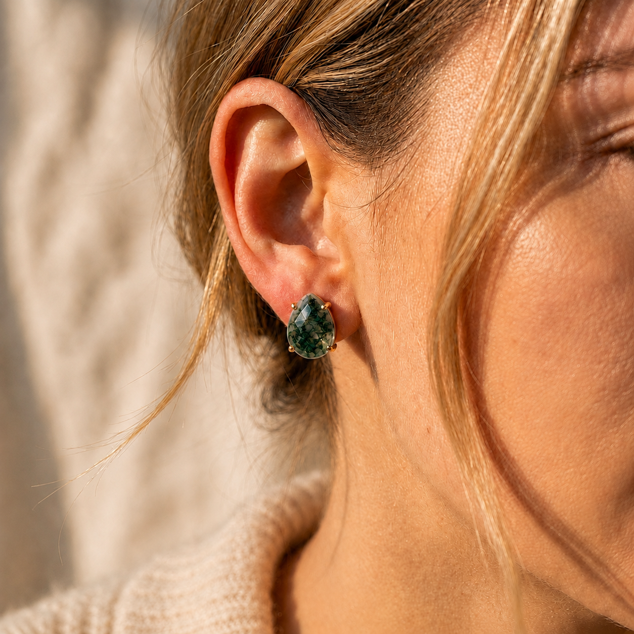 Woman wearing natural moss agate teardrop stud earring with green faceted gemstone in gold
