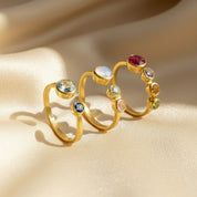 Set of custom birthstone adjustable rings for moms displayed on champagne satin, handcrafted in warm gold with smooth bezel-set gemstones. Front ring shows a two-stone design, center showcases the mom-of-two style with one larger 5mm stone and two 3mm child birthstones, and back ring highlights the mom-of-three option with one large mother stone and three smaller children’s stones. Meaningful personalized family jewelry, perfect for Mother’s Day, birthdays or Christmas gifts.