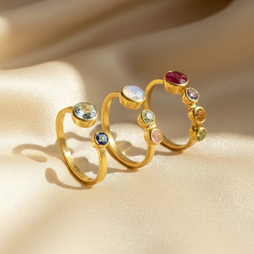 Set of multi birthstone adjustable rings for mom displayed on soft champagne satin, each handcrafted in warm gold with bezel-set gemstones in different family combinations. One ring features one large and one small birthstone, another shows a 5mm mother stone with two 3mm child stones, and the third showcases several children’s gems. These personalized family birthstone rings make meaningful gifts for moms of two or more kids for birthdays, Mother’s Day or Christmas.
