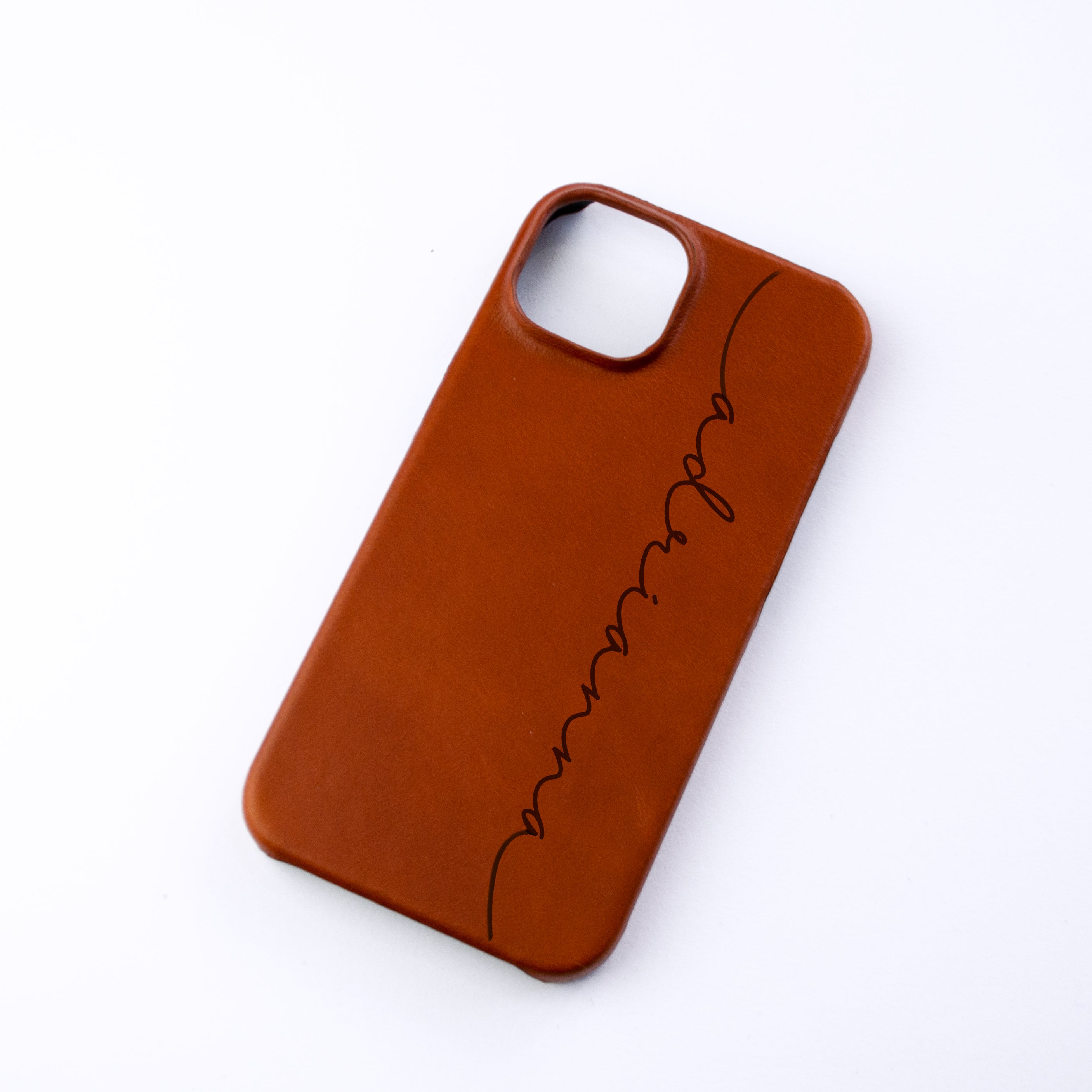 A personalized cinnamon colored phone case with the name adrianna engraved in Grace script font vertically on the case. The case rests against a white background. Engraved phone case for girlfriend, gift for daughter, personalized gift for teenage girl, customized engraved phone case for men, custom engraved phone case for women, quality leather phone case for iPhone 15