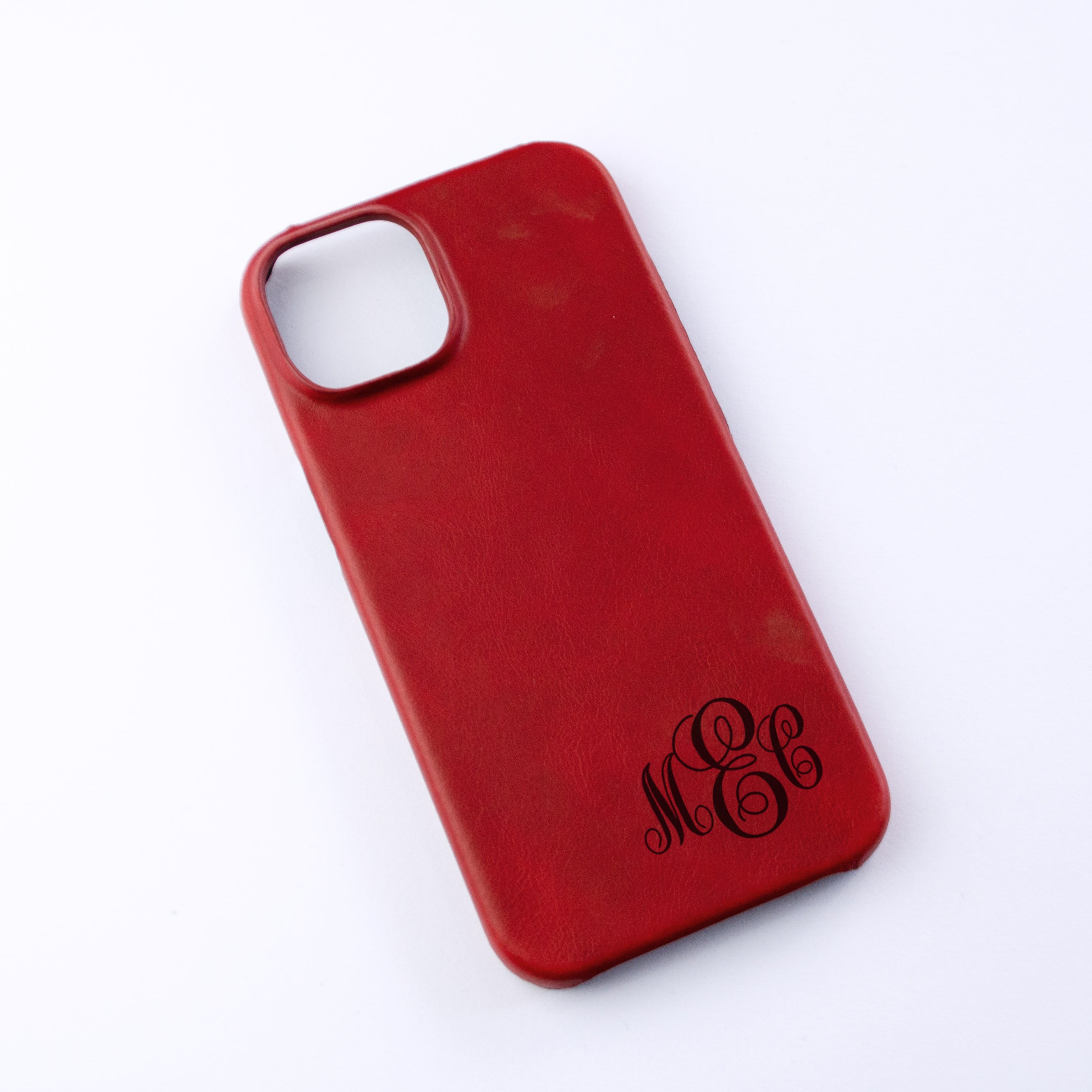 An engraved cinnamon leather iphone case rests against a white background. It is monogrammed in Swirly script  in letters MEC. Personalized leather phone case with monogram for woman, monogrammed phone case for men, gift for men, gift for person who is hard to buy for, customized leather gift.