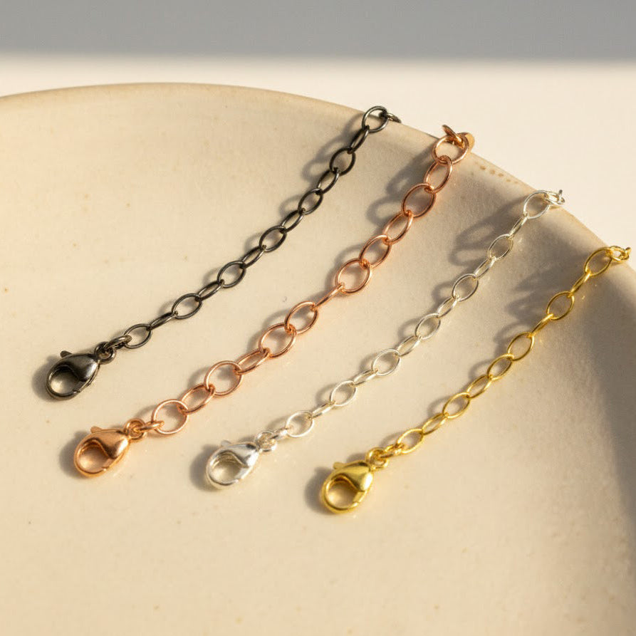 Necklace extender chains in sterling silver, gold filled, rose gold, and oxidized blackened silver displayed on a white plate. Adjustable chain extender adds 1–6 inches to necklaces or bracelets, making it perfect for layering jewelry or customizing fit. Popular jewelry accessory gift for women who love delicate, minimalist necklaces.