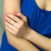 A person in a blue shirt with their hand on their arm wears a silver dog nose print ring on their middle finger.