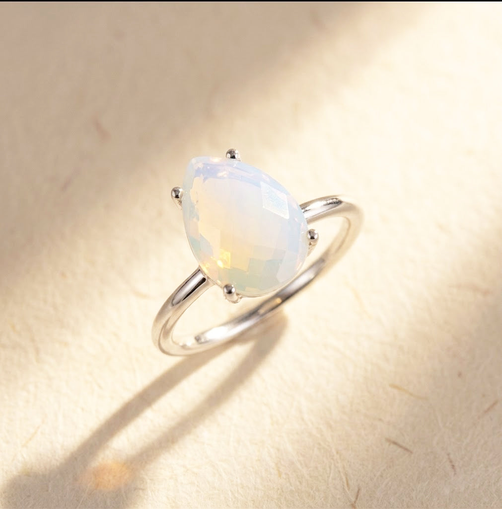 Sterling silver opalite teardrop ring shown on fabric, a dainty October birthstone ring with a pear-shaped gemstone and prong setting.