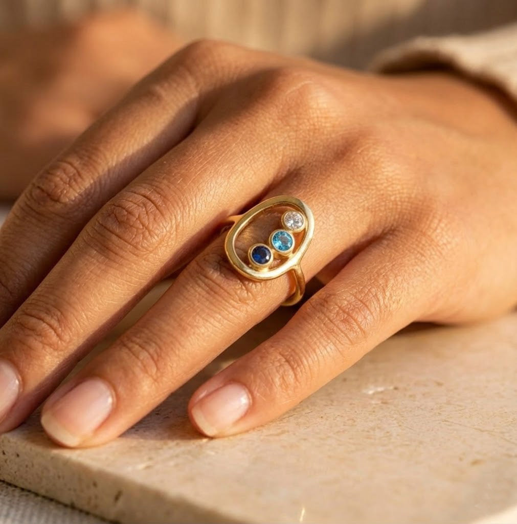 Personalized mother ring with three birthstones in open circle design on a models hand
