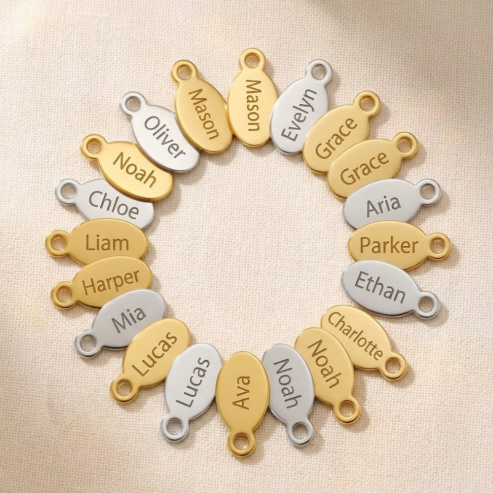 Custom oval name tag charms in gold and sterling silver with engraved names, designed as add-on charms for Danique necklaces and bracelets.
