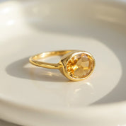 Close-up of an oval citrine gemstone ring showcasing a smooth bezel setting and polished gold band, highlighting the warm golden-yellow color of the natural citrine stone. Minimalist birthstone ring designed for stacking or wearing alone, ideal as a November birthstone gift, dainty gemstone ring for women, and personalized jewelry for moms, daughters, and partners. Perfect for everyday wear, birthdays, anniversaries, and sentimental gifting.