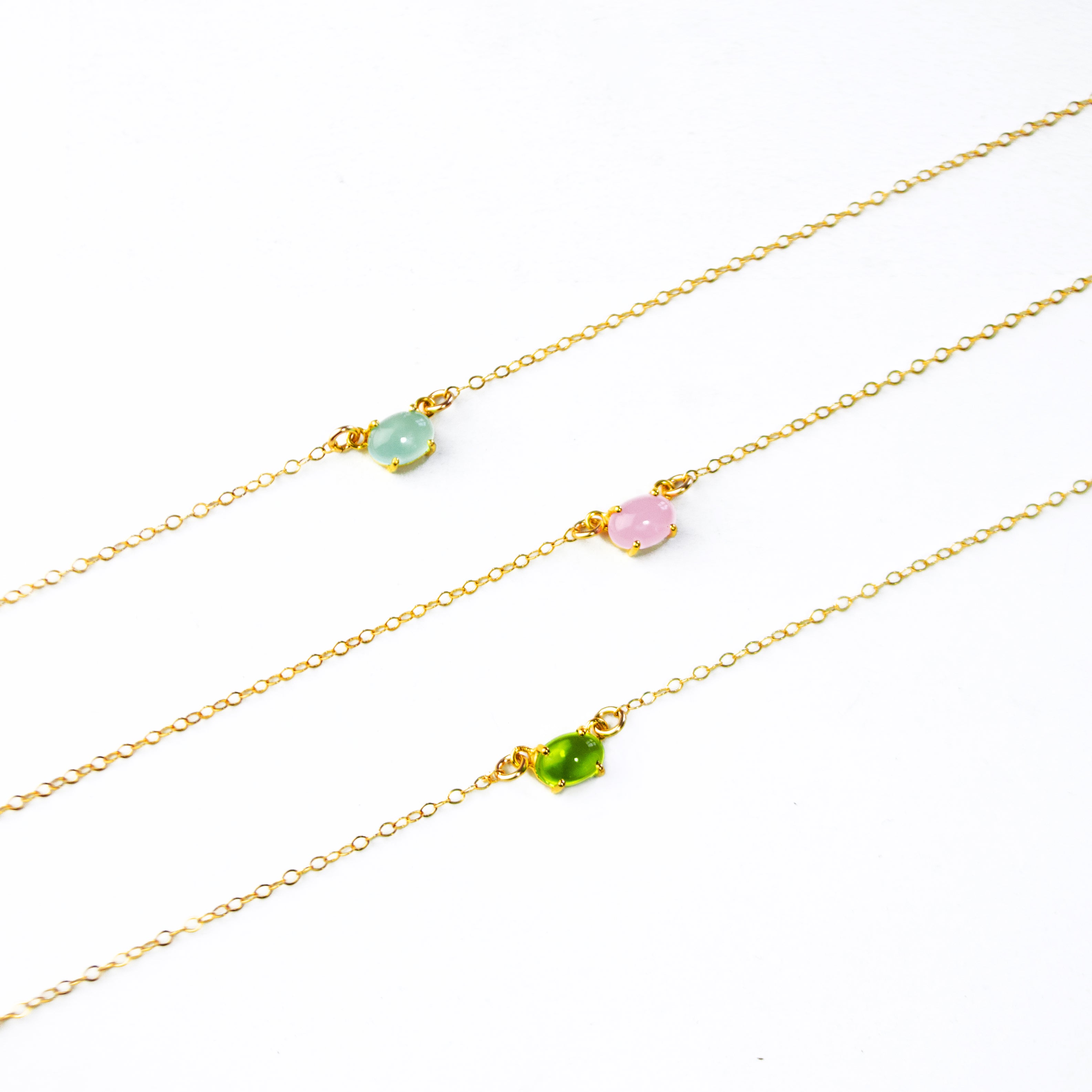 Three oval cabochon birthstone prong set necklaces featuring aqua chalcedony, pink chalcedony and peridot. 