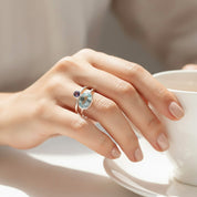 Close-up hand wearing a personalized birthstone stacking ring set, dainty bezel gemstone rings with a larger oval stone for mom and tiny round stones for children, minimalist mothers ring set in gold vermeil or sterling silver, custom family jewelry gift for mom of two, mom of three, or grandma, choose January garnet and March aquamarine combinations by birth month, delicate stacking rings for everyday wear