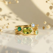 Stacking birthstone ring set for mom and kids in 18K yellow gold vermeil, custom family ring set with large oval stone for mom and tiny round birthstones for children, minimalist dainty stacking rings photographed with soft florals and warm light, meaningful mothers ring set and grandma gift, personalize with January garnet, May emerald, and December blue topaz birthstones, keepsake family jewelry