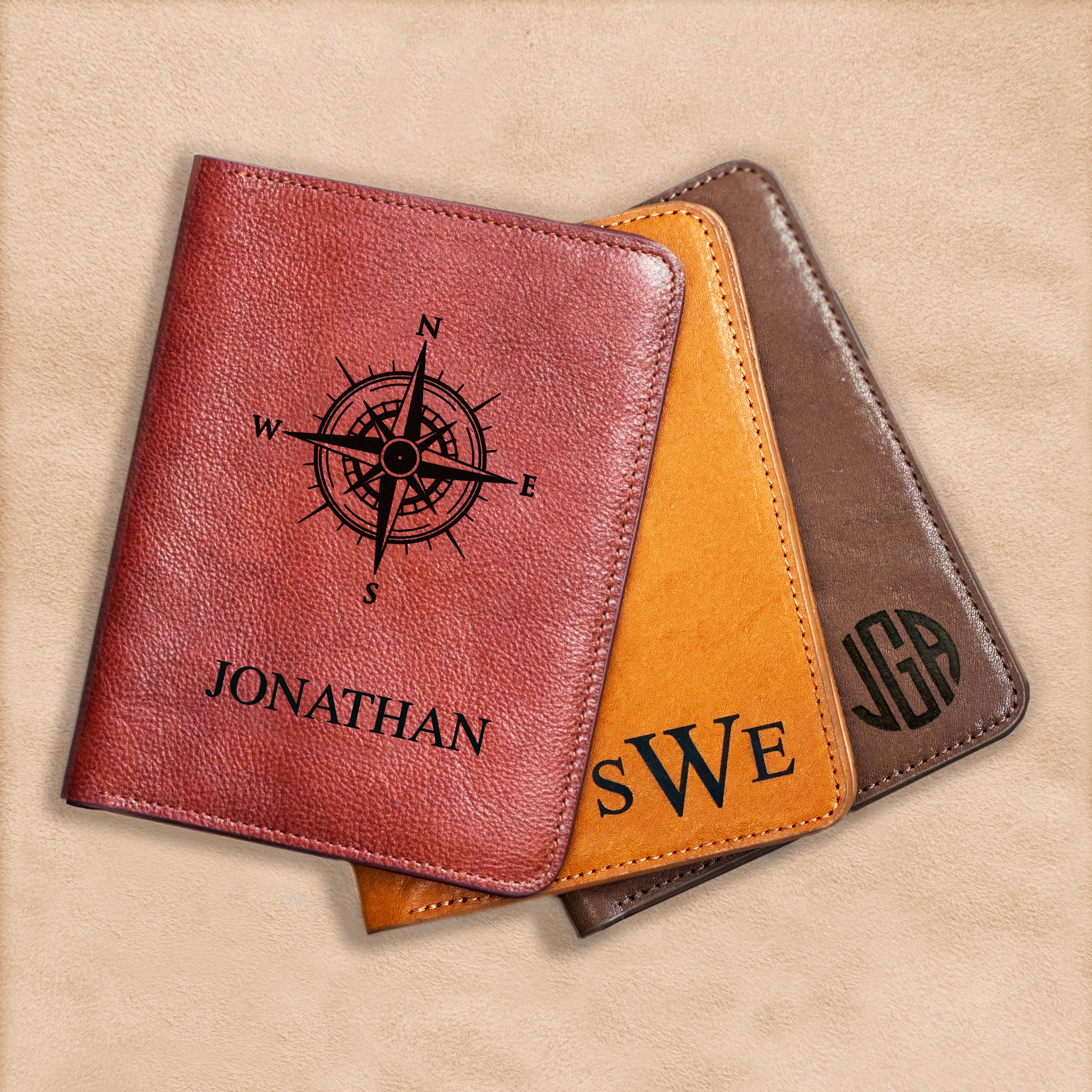 Three Natural Leather passport holders in rich cinnamon, sweet honey and earthy espresso rest against a natural wood background. Each passport sleeve is custom Monogrammed and engraved. The cinnamon passport holder has a compass and the name Jonathan in Classic font. The honey has the intials SWE engraved in our Timeless Monogram format. The espresso passport cover is engraved with the initials JGA in our Spherical Monogram format.