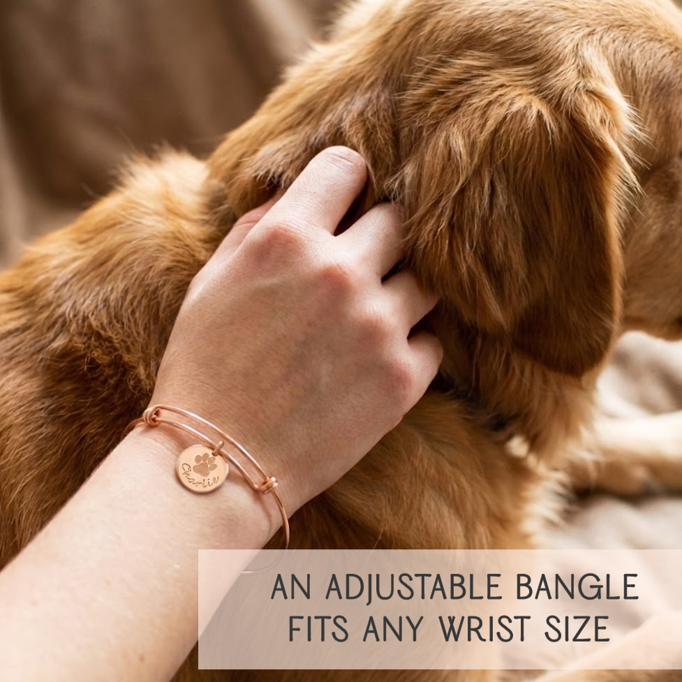 Personalized pet bangle bracelet worn by a woman hugging her dog, highlighting engraved paw print and custom pet name on a polished disc charm. Perfect meaningful jewelry gift for dog moms, pet lovers, or anyone wanting a sentimental keepsake. Adjustable wire bangle crafted in sterling silver, gold, or rose gold. Ideal for birthdays, holidays, Mother’s Day, and memorial pet gifts, offering heartfelt symbolism and everyday wear comfort.