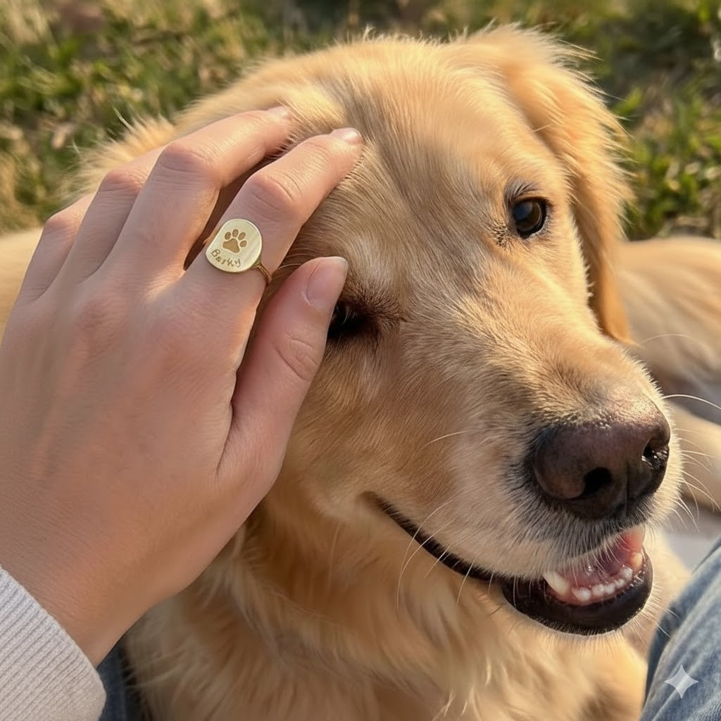 Cozy lifestyle scene of a woman sitting with her black dog, wearing her custom paw print ring as she pets their head, showing how the dainty engraved disc ring is an everyday reminder of her pup. Personalized pet memorial jewelry and dog mom gift idea, custom paw print ring that celebrates the bond with a beloved pet, ideal for birthdays, holidays or remembrance.