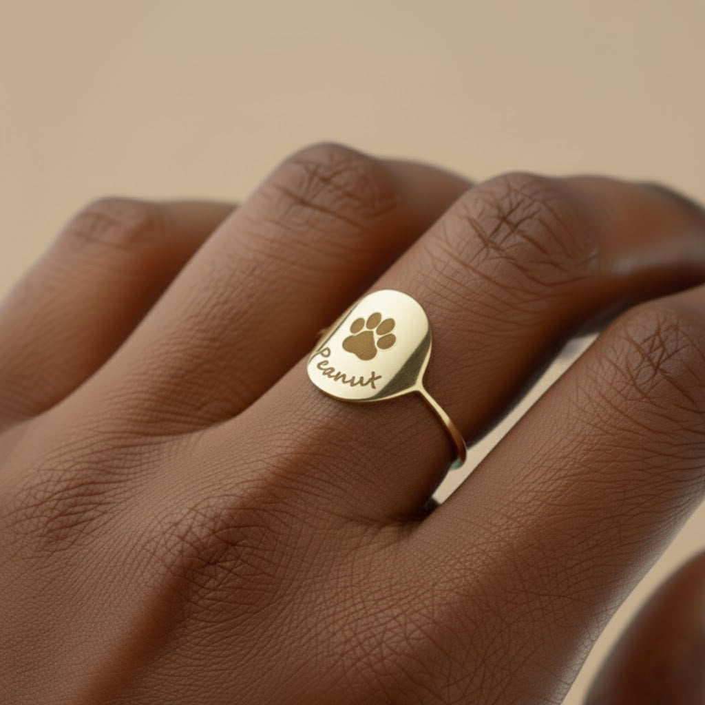 Custom engraved paw print ring in shiny yellow gold vermeil shown on a woman’s hand, featuring a round disc engraved with a centered dog paw and pet name beneath, minimalist band perfect for stacking. Personalized pet memorial ring keeps your cat or dog close every day, thoughtful dog mom gift or pet lover jewelry for birthdays, Christmas, Mother’s Day or to remember a beloved pet.