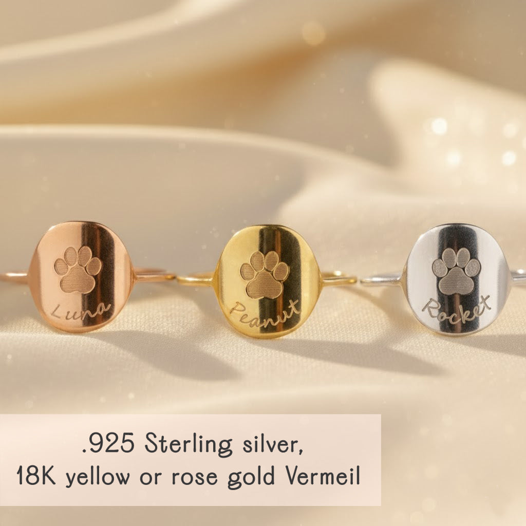 Row of three custom engraved paw print rings displayed on soft champagne satin, showing .925 sterling silver, 18K yellow gold vermeil and rose gold vermeil finishes with centered paw prints and optional pet names. Personalized dog or cat paw print ring for pet lovers, stackable band that works as a memorial ring or everyday dog mom ring, perfect gift for birthdays, Christmas or pet loss sympathy.