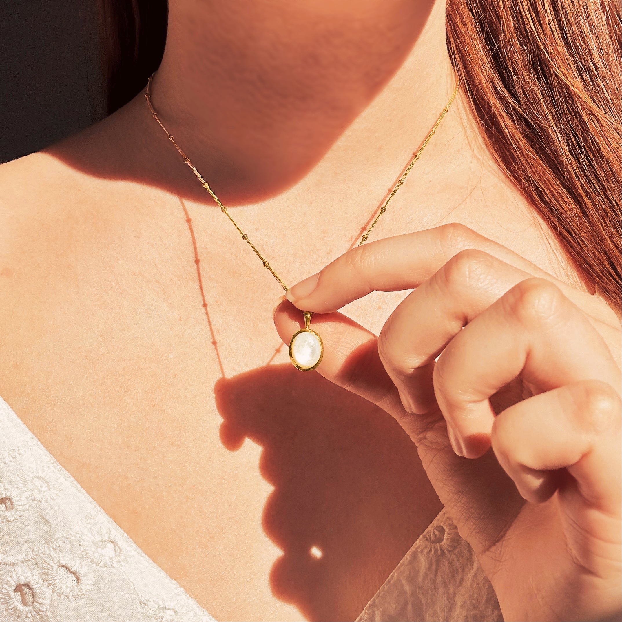 Model wearing a white lace blouse holds Dainty Large Oval Mother of Pearl Bezel Set Pendant on a gold filled satellite chain. Pearl Bridal Jewelry Necklace, Natural Mother of Pearl Seashell, Seashell Jewelry, Ocean Jewelry, Summer Birthday