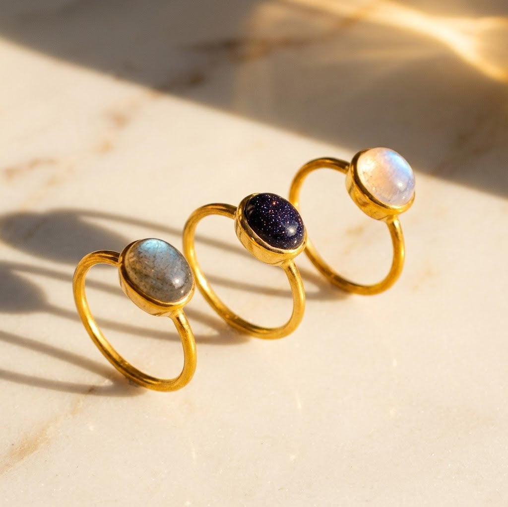 Stackable oval gemstone rings featuring rainbow moonstone, labradorite, sunstone and other colorful birthstones in gold settings.