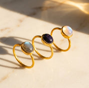 Stackable oval gemstone rings featuring rainbow moonstone, labradorite, sunstone and other colorful birthstones in gold settings.