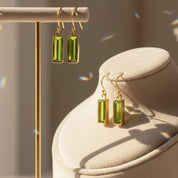 Gold peridot bar earrings displayed on a minimalist jewelry stand