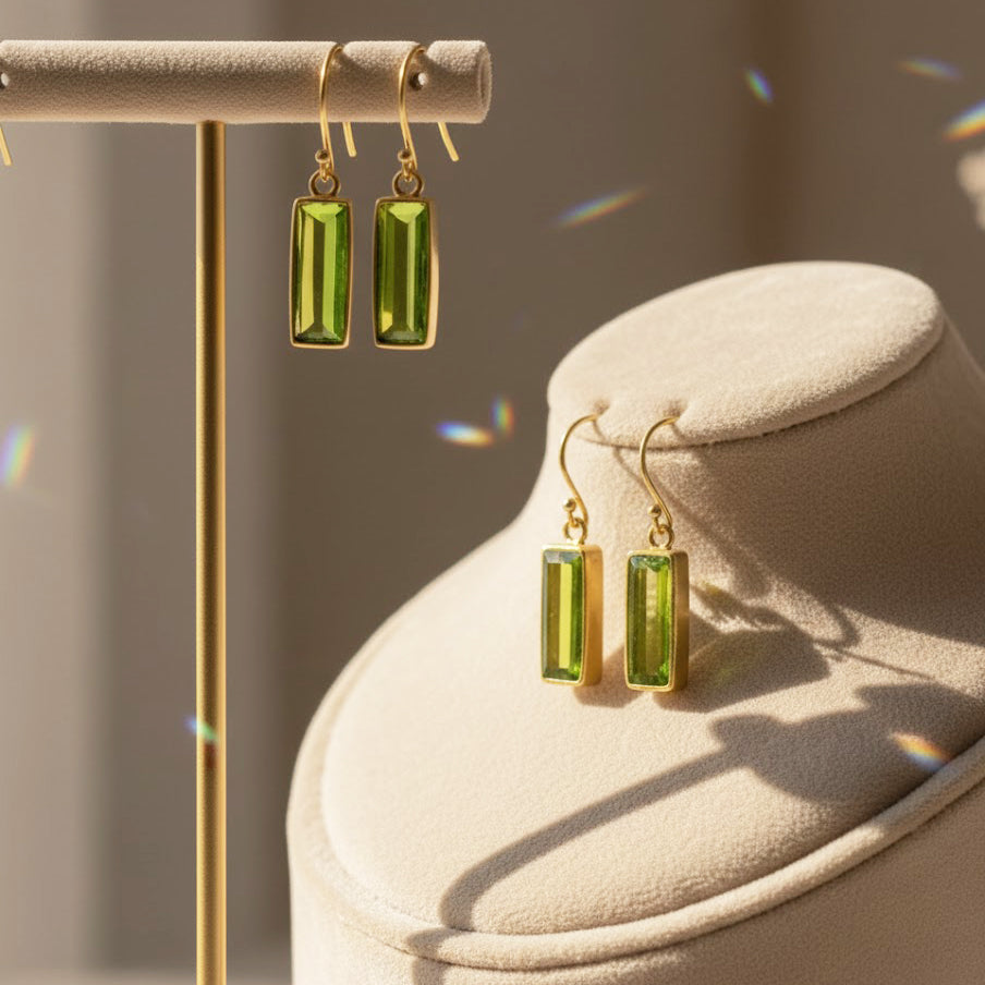 Gold peridot bar earrings displayed on a minimalist jewelry stand