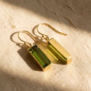 Pair of gold peridot baguette earrings resting on sunlit beige linen