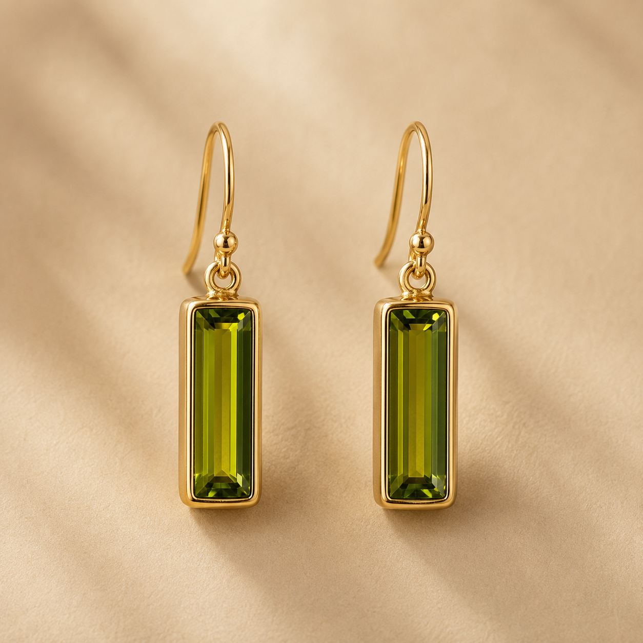 Gold peridot baguette drop earrings hanging against a warm beige background