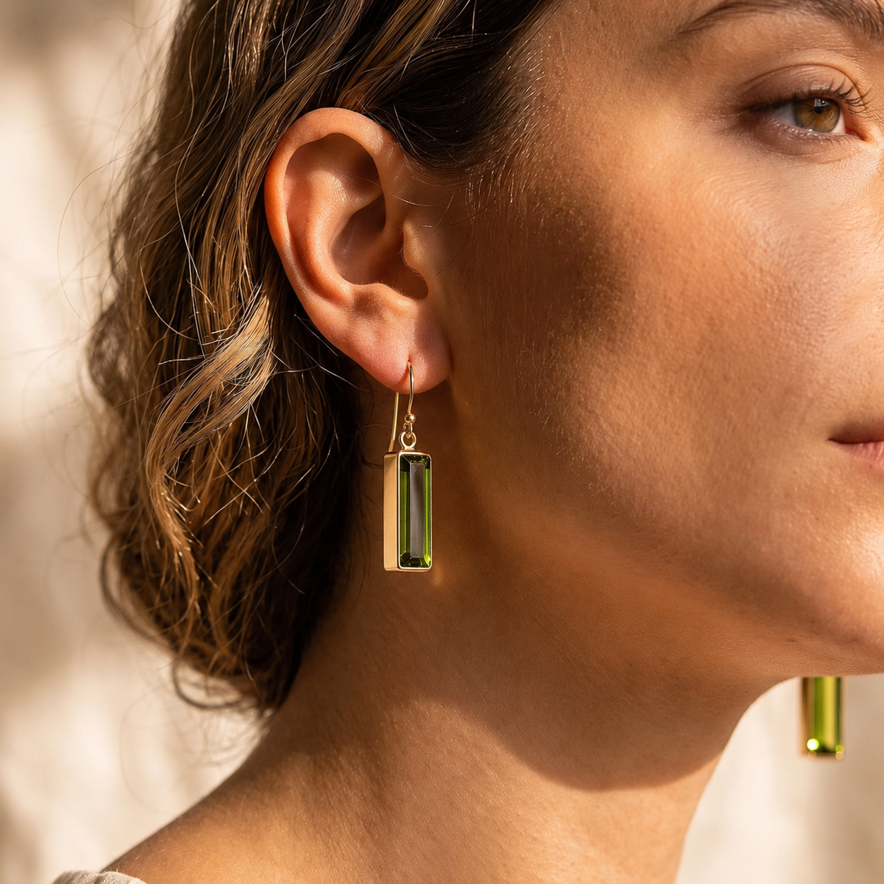 Close-up of a model wearing gold peridot baguette earrings