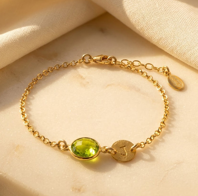Personalized gold peridot initial bracelet with round faceted August birthstone and engraved disc charm.