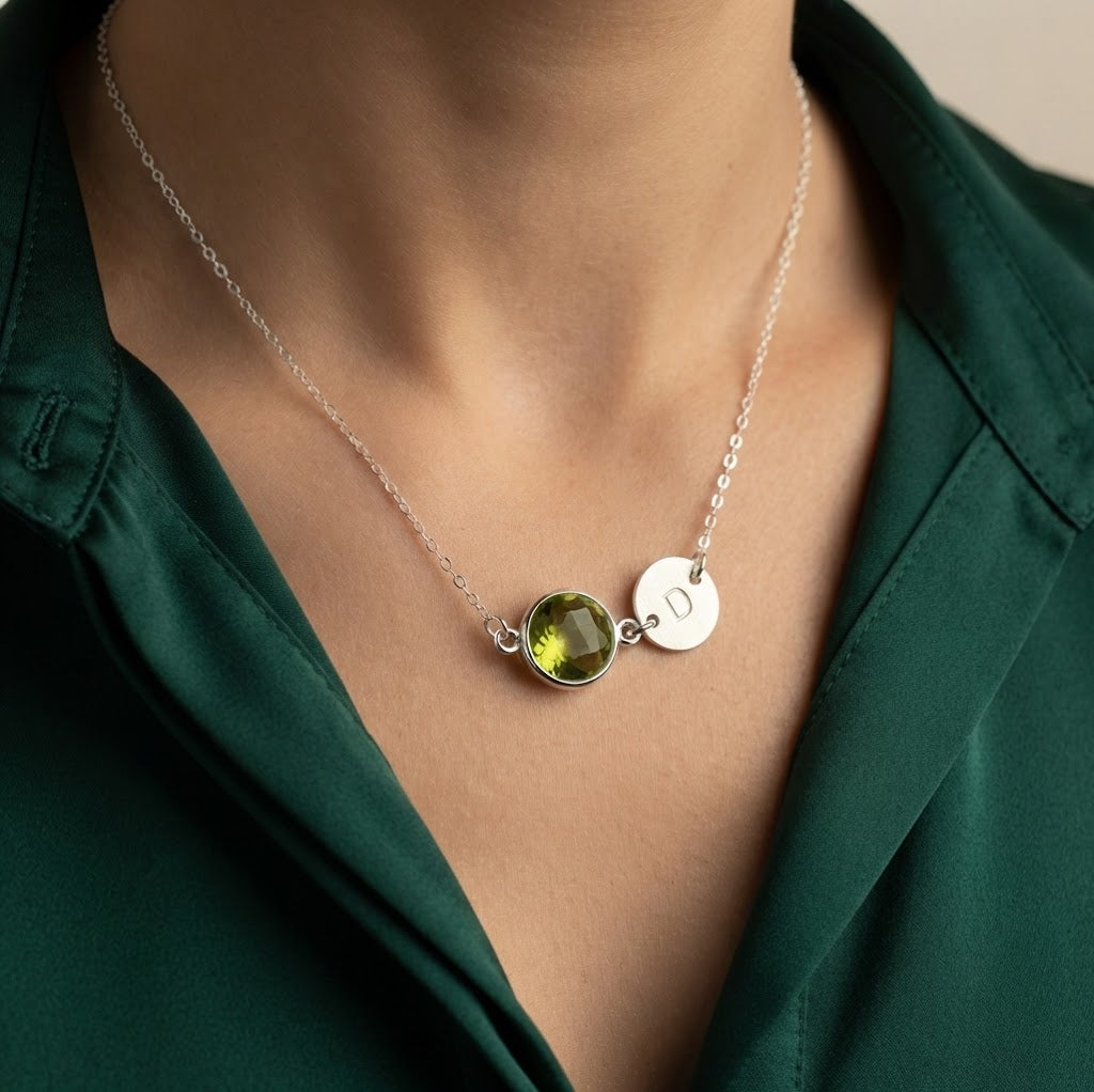 Sterling silver Peridot initial necklace worn by a woman with round green August birthstone and stamped charm