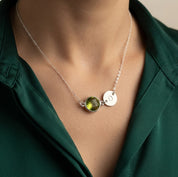 Sterling silver Peridot initial necklace worn by a woman with round green August birthstone and stamped charm